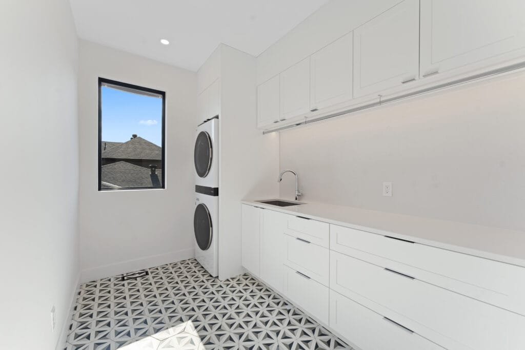 Bright laundry room from Stone Design Concepts portfolio Bespoke Developments Dunblane Project, featuring patterned flooring, white cabinetry, and a stacked washer-dryer.