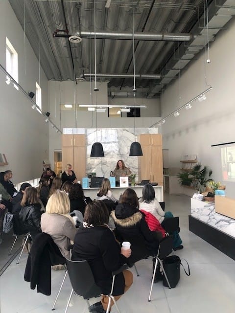 Audience attentively listening to a speaker at the Cosentino event Stone Design Concepts, held in a stylish showroom with marble and wood accents.
