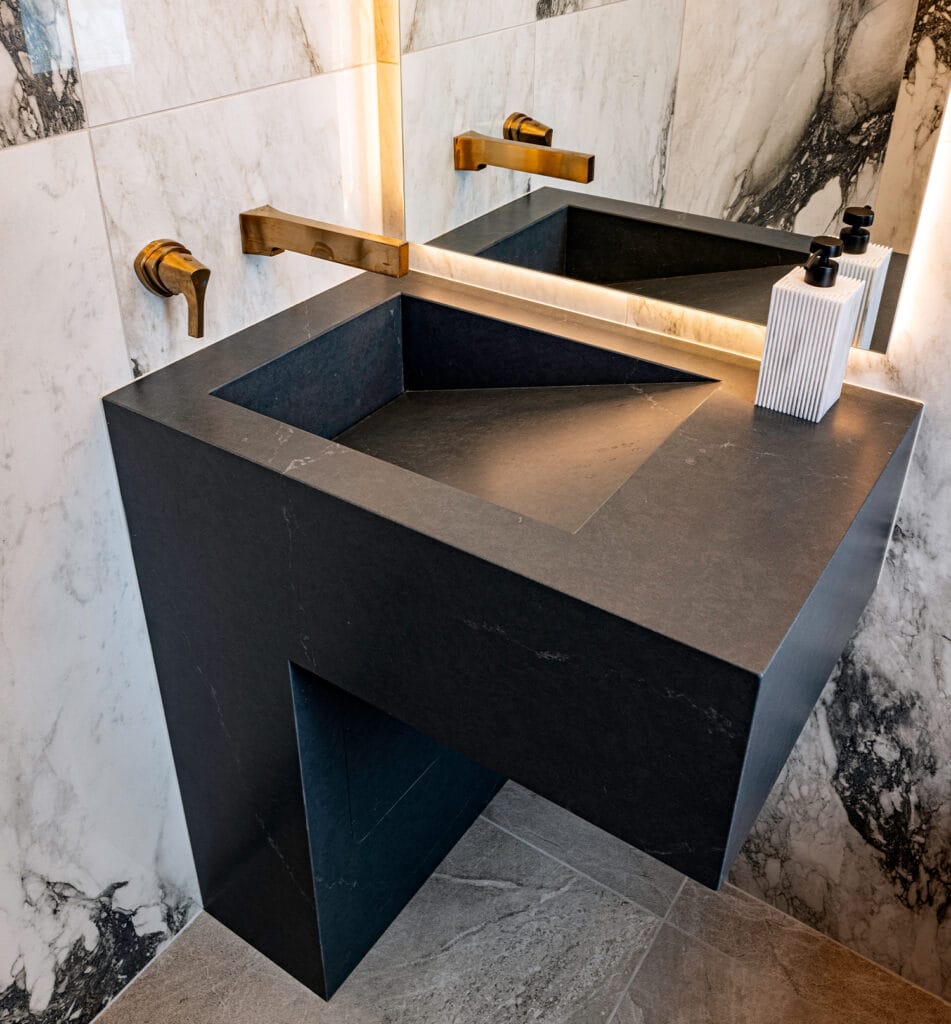 Modern bathroom setup featuring a Stone Design Concepts Sink and Shower Products black stone sink with sleek brass fixtures and dramatic marble wall accents.